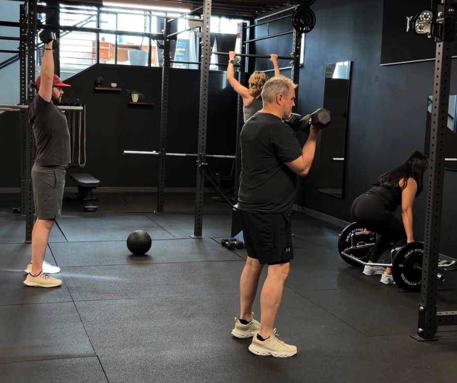 Small group personal training session in Denver with clients performing strength exercises under coach supervision.